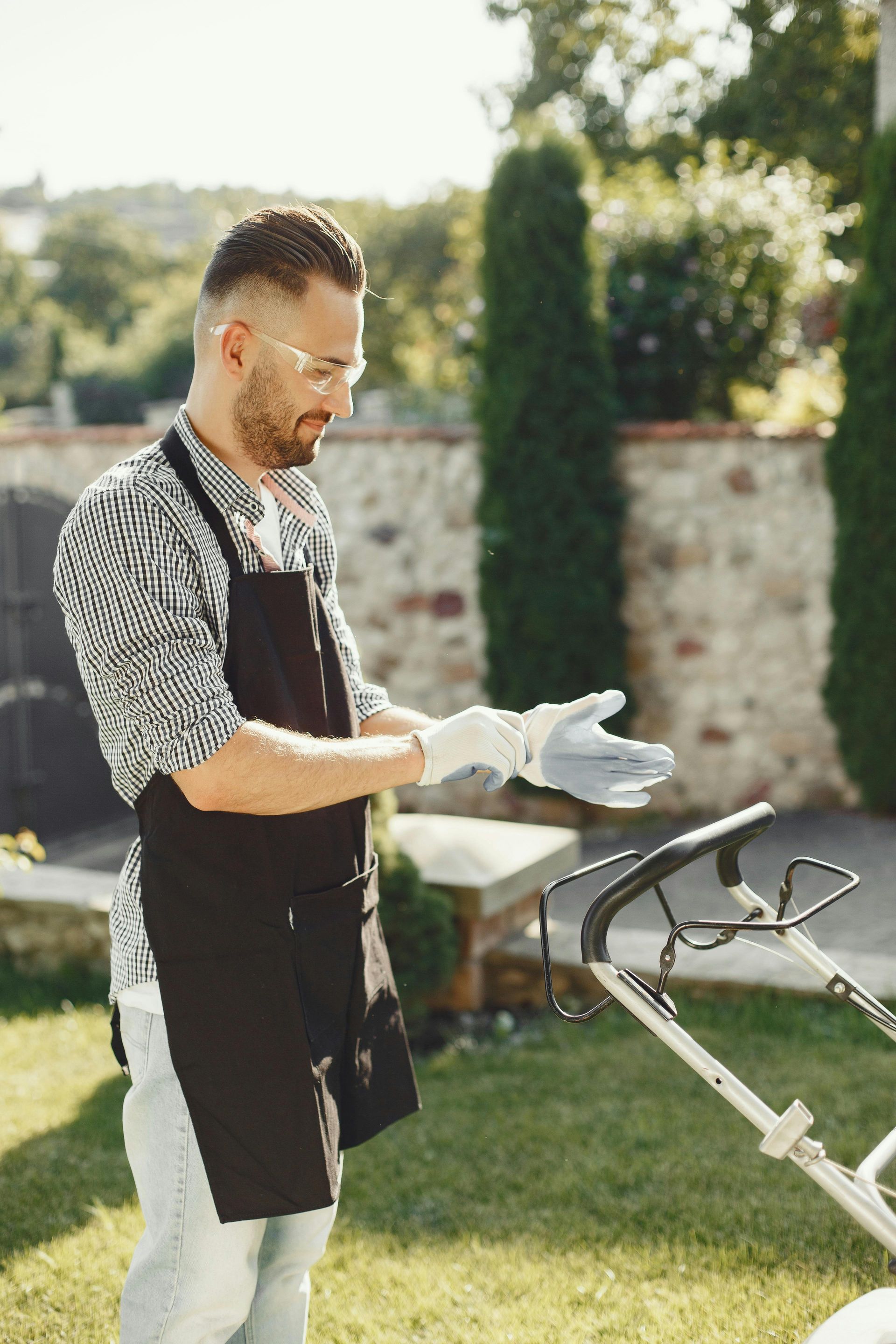 A man in gloves and apron prepares to mow the lawn on a sunny day.